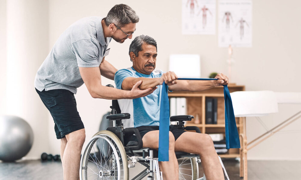 Smiling friendly in-home male nurse in uniform supporting an old man with a walking stick